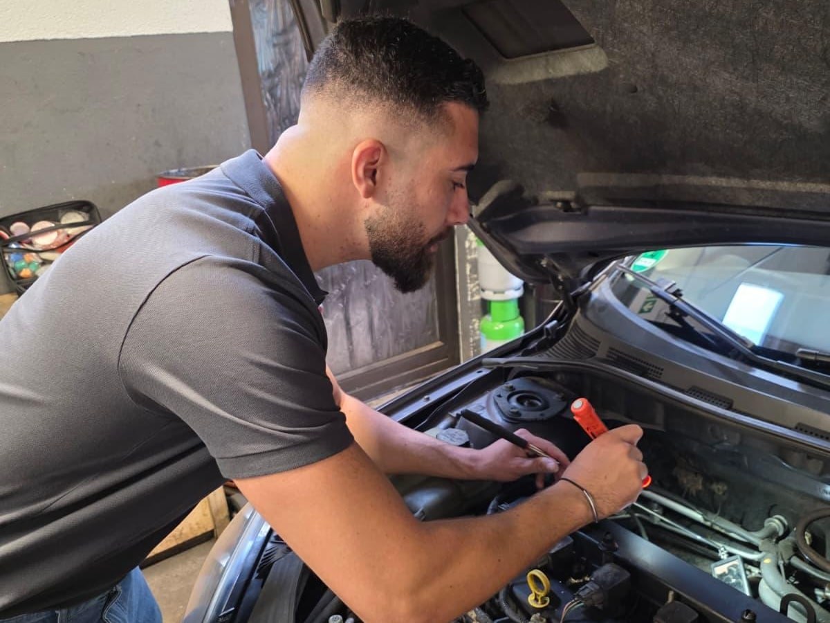 Josha Schumacher prüft mit einer Leuchte Bauteile im geöffneten Motorraum
