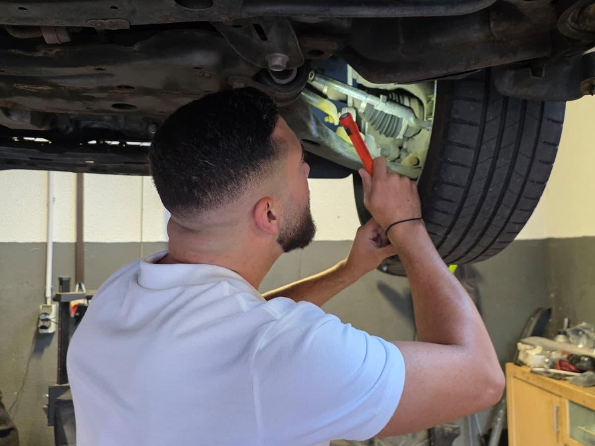 Josha Schumacher prüft Unterboden und Fahrwerk eines angehobenen Fahrzeugs auf der Hebebühne
