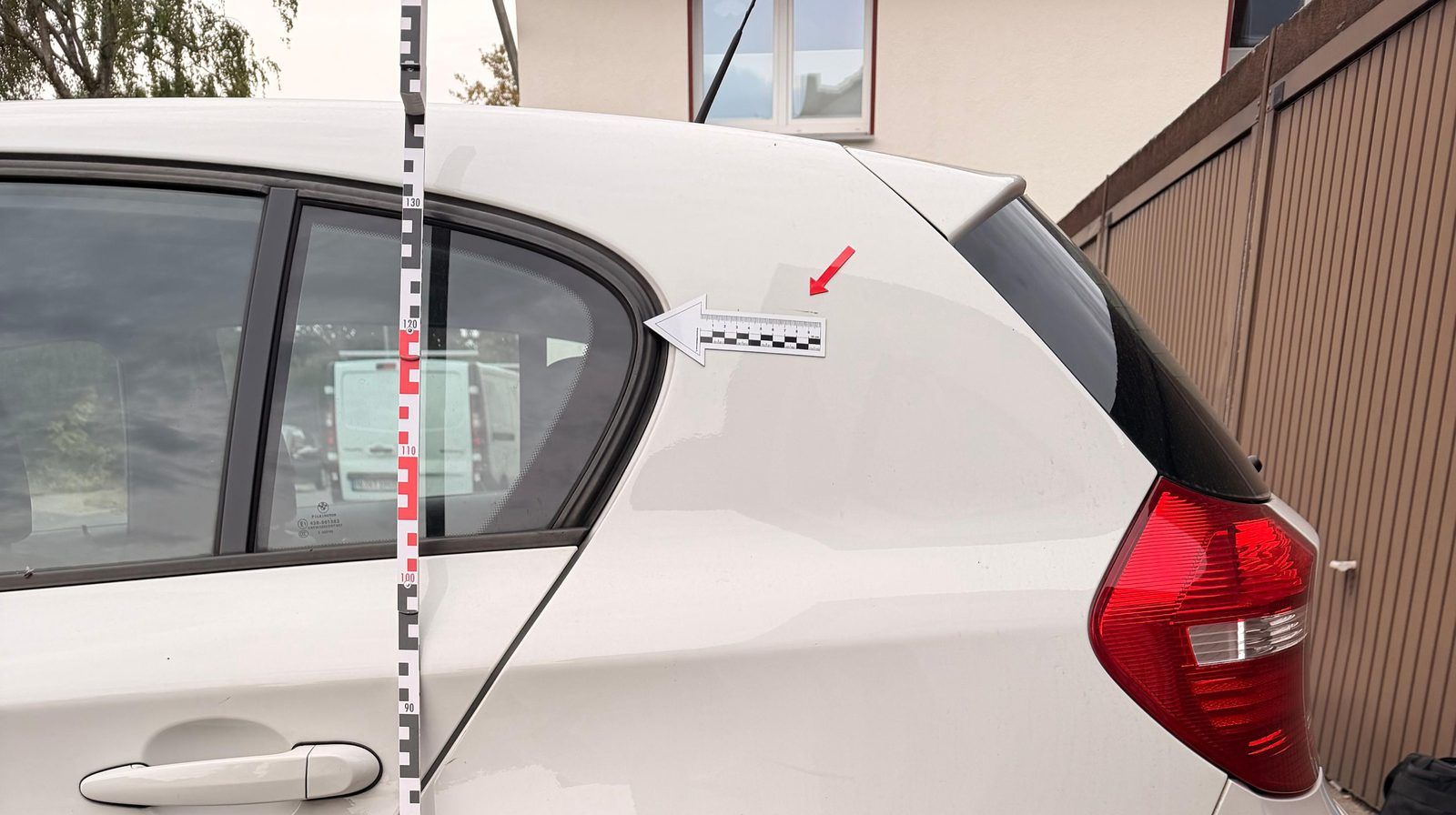 Beschädigte Seite eines weißen BMW mit Messlatte und Pfeilmaßstab am Schaden